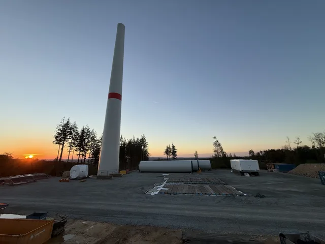 Sonnenuntergang neben einem Windradturm und gelagerten Bauteilen