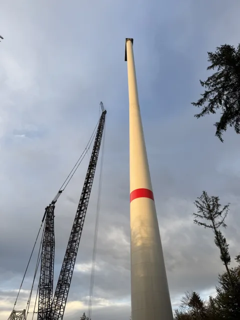 Windradturm und Kran im goldenen Licht vor grauen Wolken